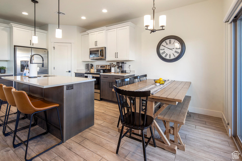 Kitchen featuring appliances with stainless steel finishes, light wood finished floors, a kitchen bar, recessed lighting, and white cabinets