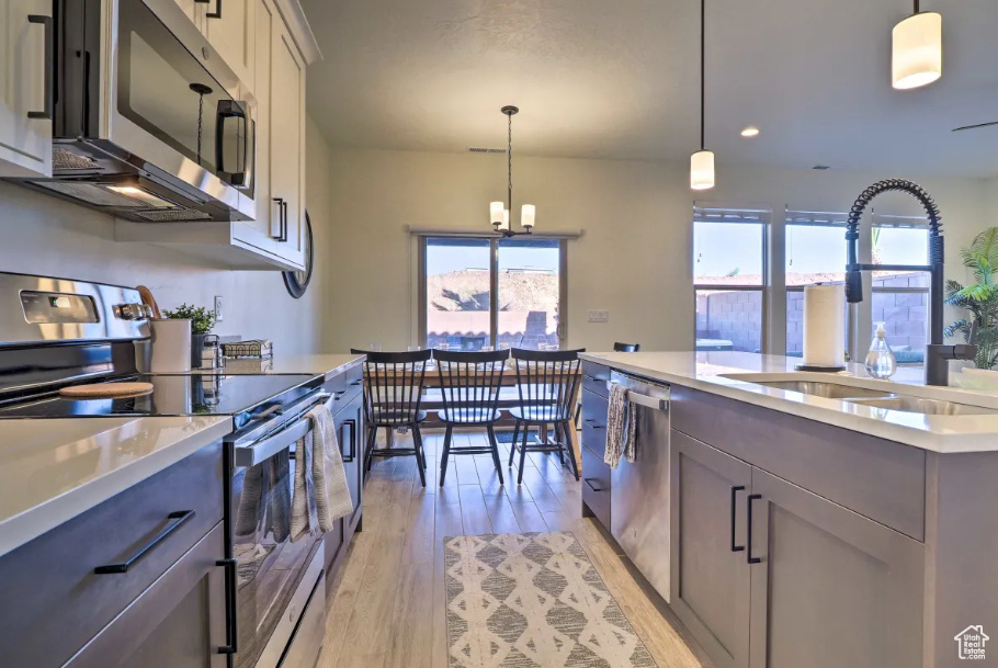 Kitchen featuring stainless steel appliances, light countertops, light wood-style floors, a chandelier, and pendant lighting