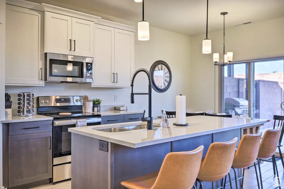 Kitchen featuring stainless steel appliances, light countertops, a kitchen island with sink, a kitchen bar, and decorative light fixtures