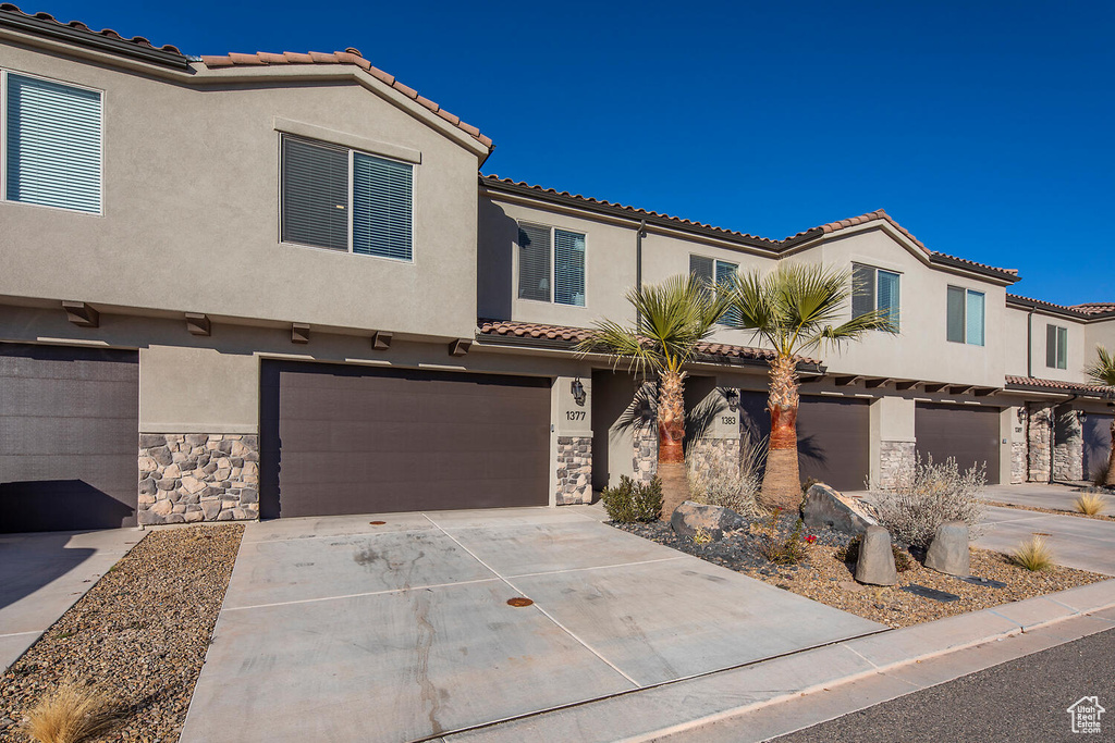View of front facade featuring a garage, concrete driveway, stone siding, a tiled roof, and stucco siding