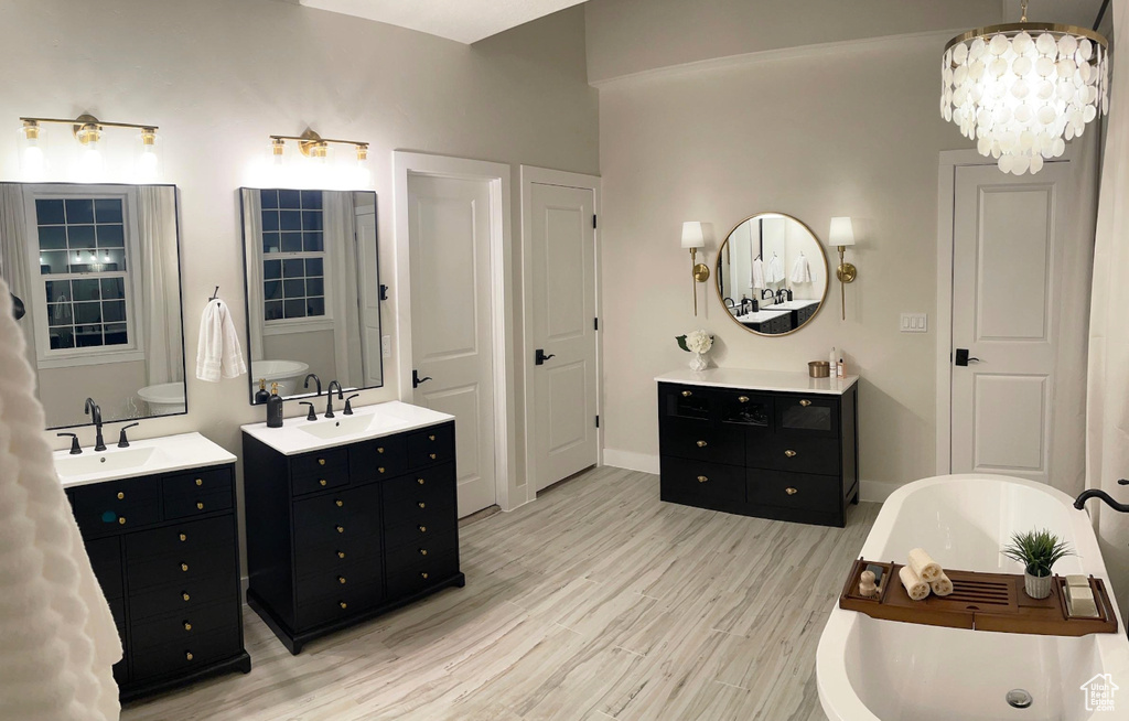 Full bathroom featuring two vanities, wood finished floors, a freestanding bath, and a chandelier