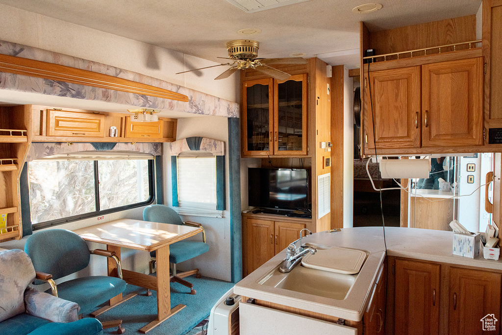 Kitchen featuring a ceiling fan, brown cabinets, light countertops, carpet flooring, and glass insert cabinets