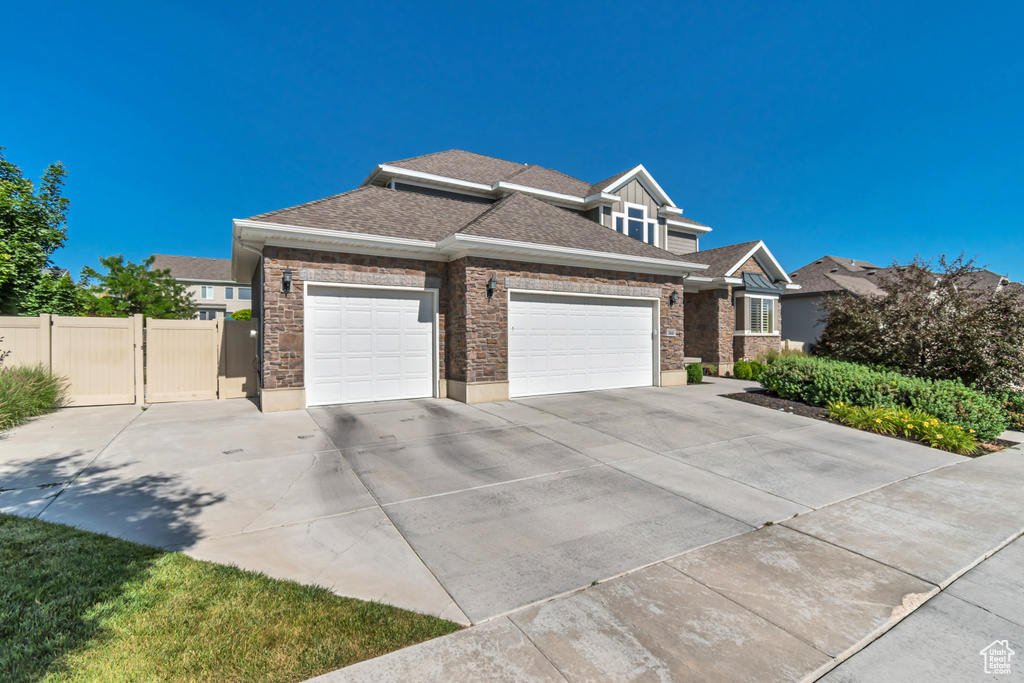 View of front of house with an attached garage, driveway, stone siding, and a shingled roof