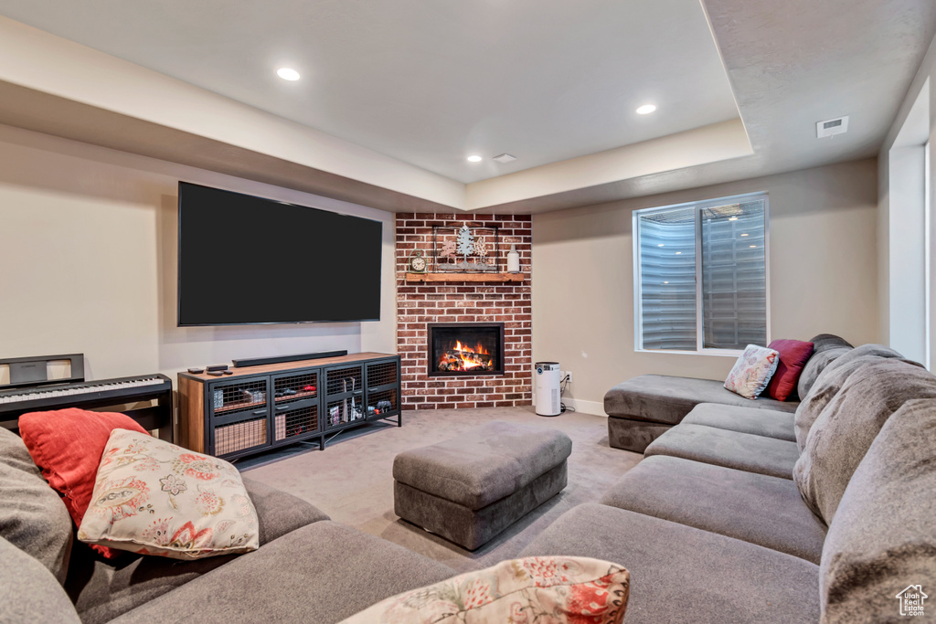 Living room with a brick fireplace, carpet flooring, recessed lighting, and a raised ceiling