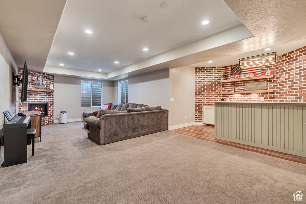 Living room with a fireplace, a tray ceiling, carpet flooring, recessed lighting, and brick wall