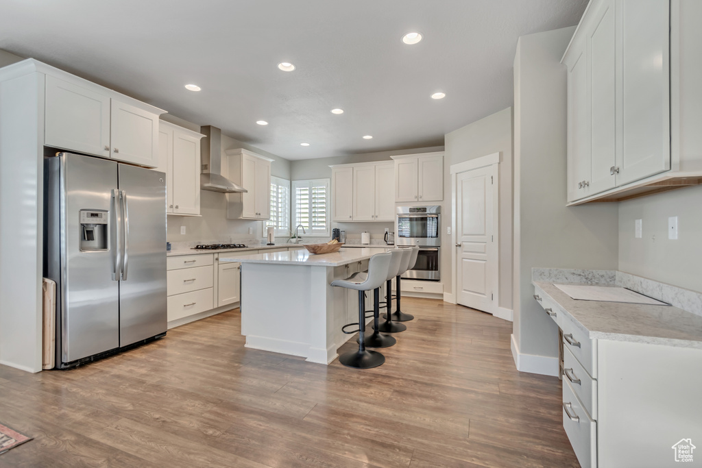 Kitchen with stainless steel appliances, wall chimney range hood, a breakfast bar, recessed lighting, and white cabinetry