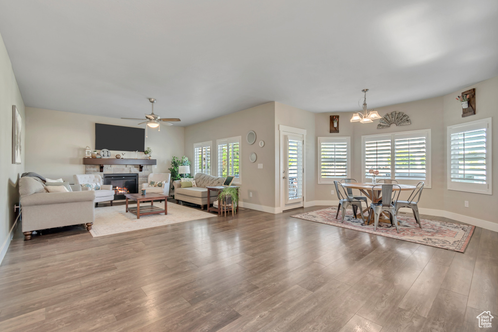 Living area with a stone fireplace, a chandelier, wood finished floors, and ceiling fan