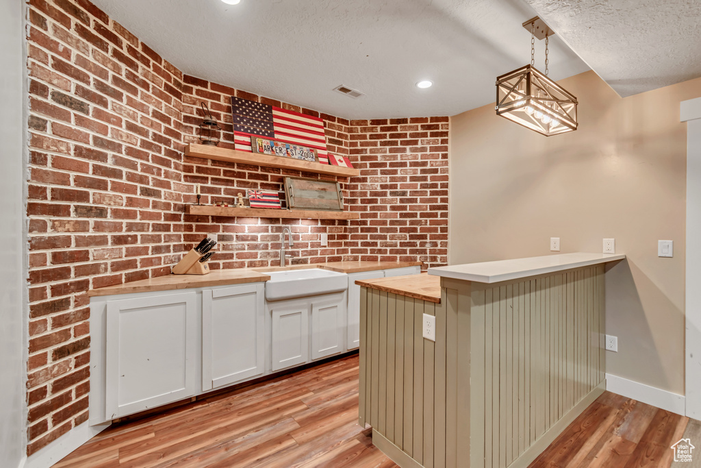 Kitchen featuring butcher block counters, open shelves, light wood-style flooring, decorative light fixtures, and a textured ceiling