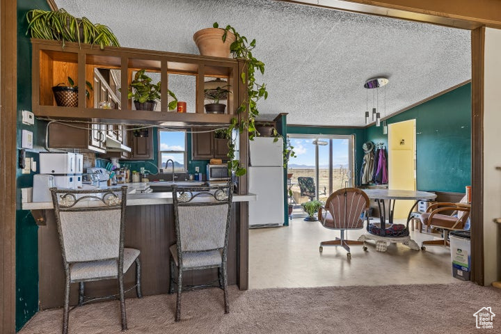 Kitchen with freestanding refrigerator, stainless steel microwave, a textured ceiling, plenty of natural light, and a breakfast bar