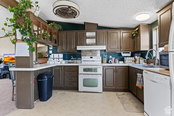 Kitchen with white appliances, light countertops, a peninsula, under cabinet range hood, and a textured ceiling