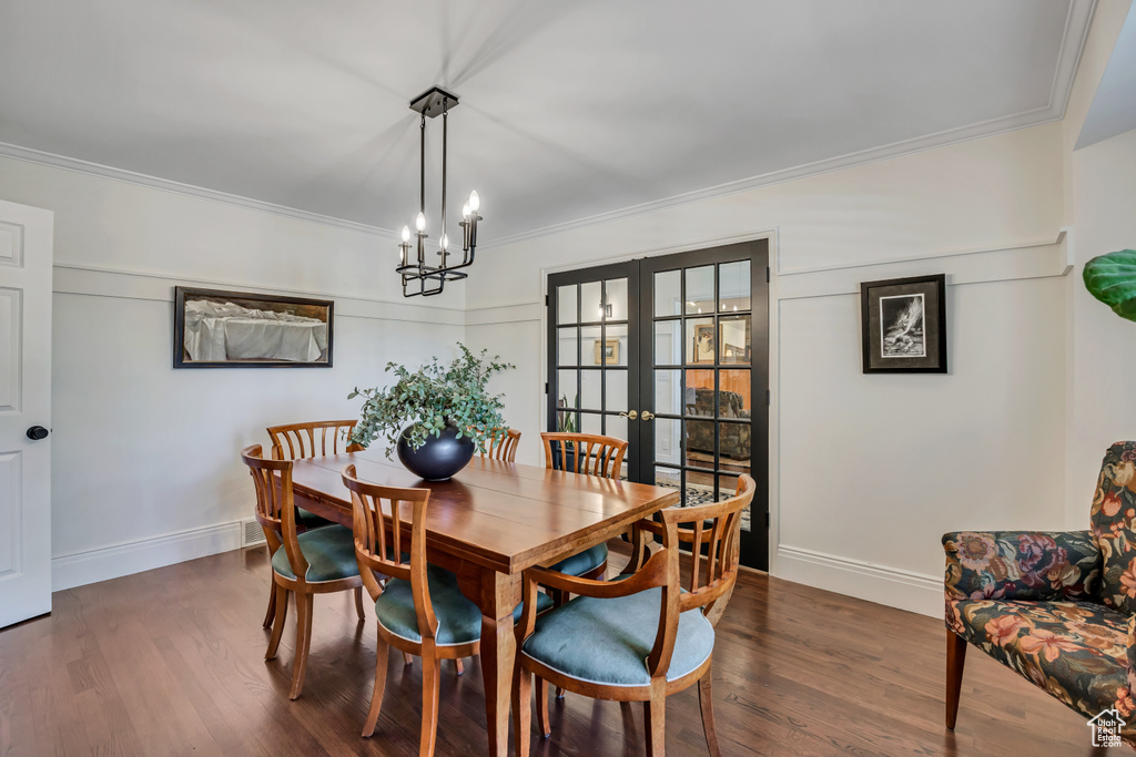 Dining space featuring crown molding, dark wood-style floors, a chandelier, and french doors