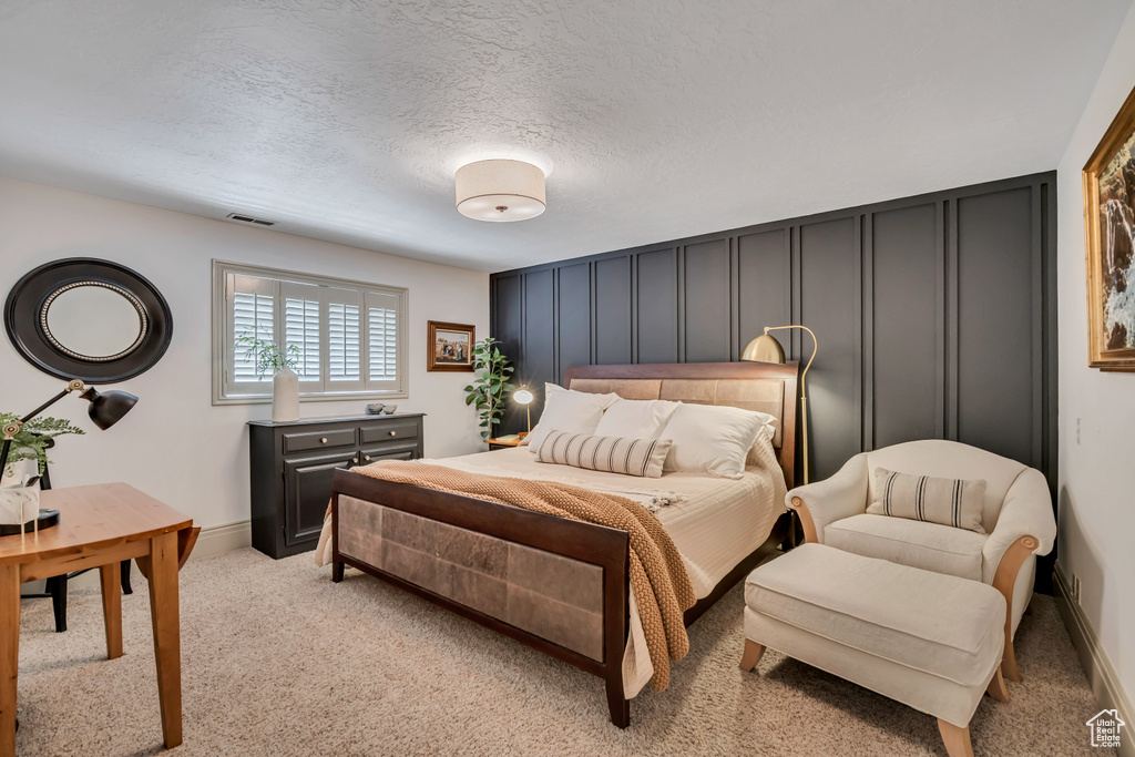 Bedroom with light carpet, a decorative wall, and a textured ceiling