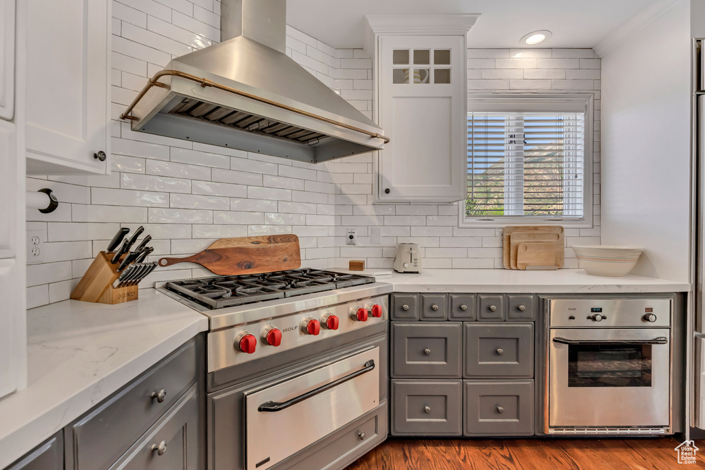Kitchen featuring wall chimney exhaust hood, stainless steel appliances, gray cabinetry, a warming drawer, and backsplash