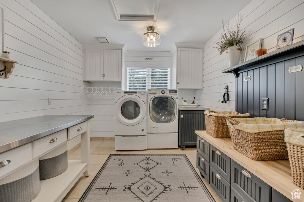 Laundry area featuring cabinet space, washer and clothes dryer, wood walls, and light tile patterned floors