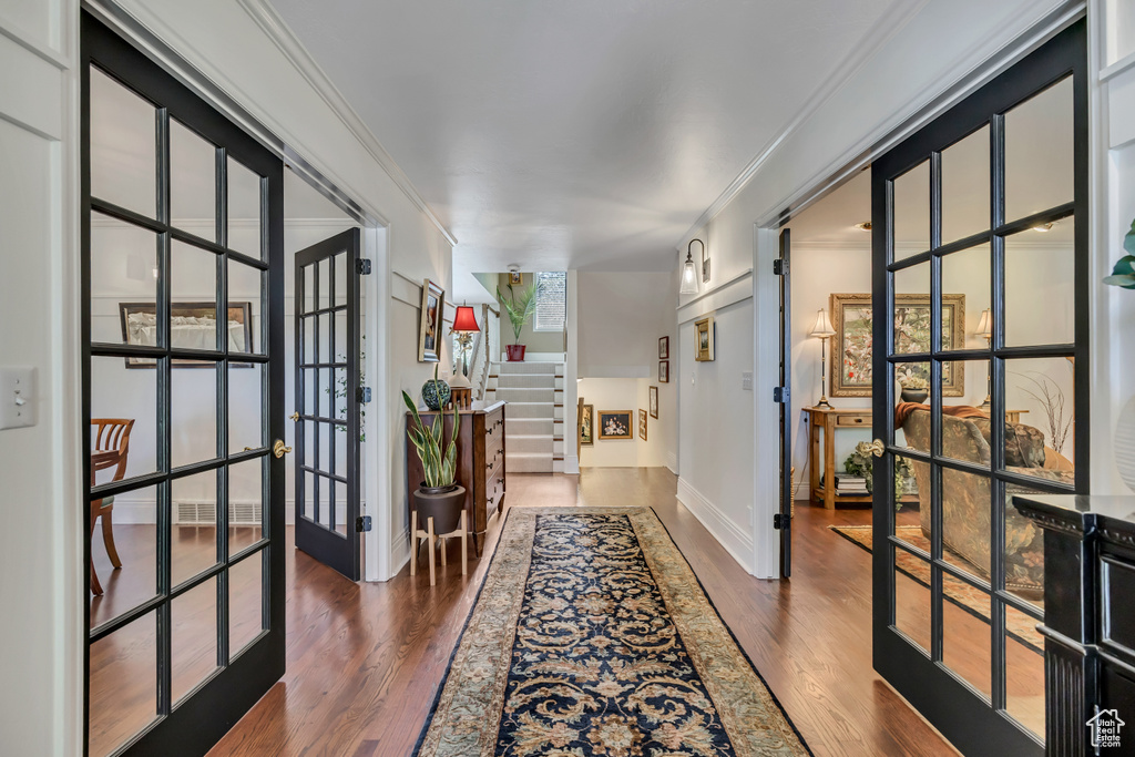 Corridor with french doors, dark wood-type flooring, crown molding, and stairway