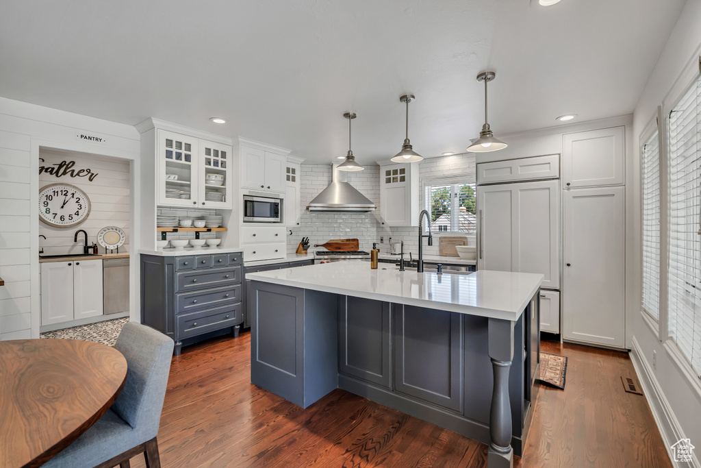 Kitchen with stainless steel microwave, gray cabinetry, backsplash, light countertops, and wall chimney range hood