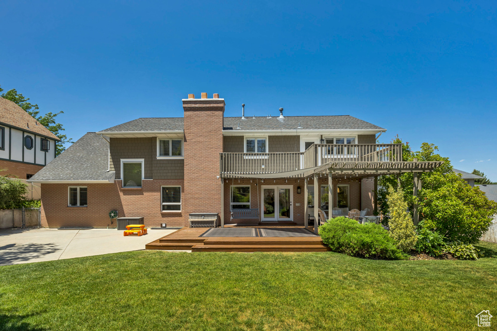 Rear view of house with a chimney, a deck, a patio, brick siding, and roof with shingles