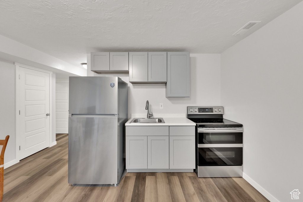 Kitchen featuring stainless steel appliances, gray cabinets, light wood-style floors, light countertops, and a textured ceiling