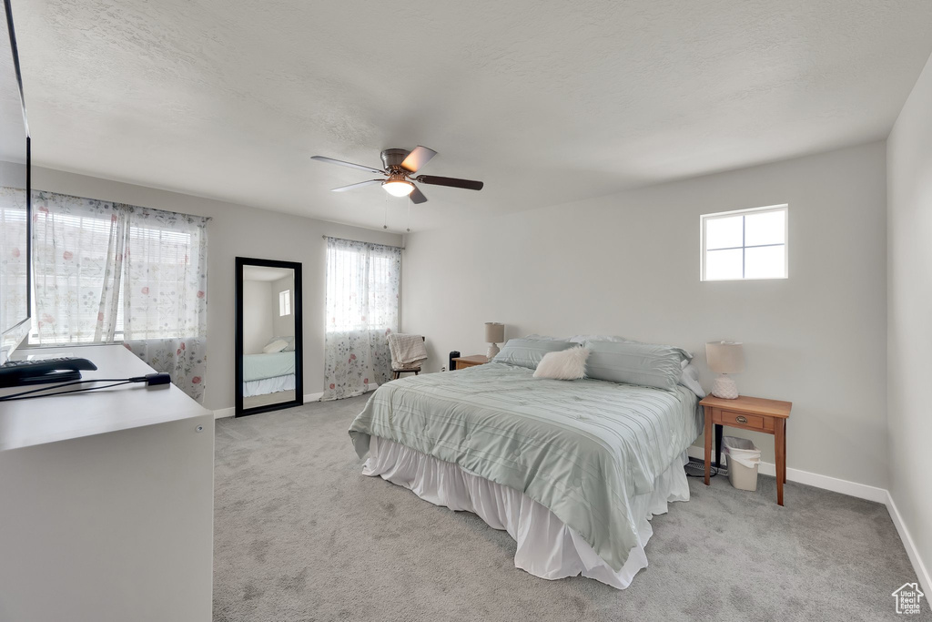 Bedroom featuring multiple windows, light colored carpet, ceiling fan, and a textured ceiling