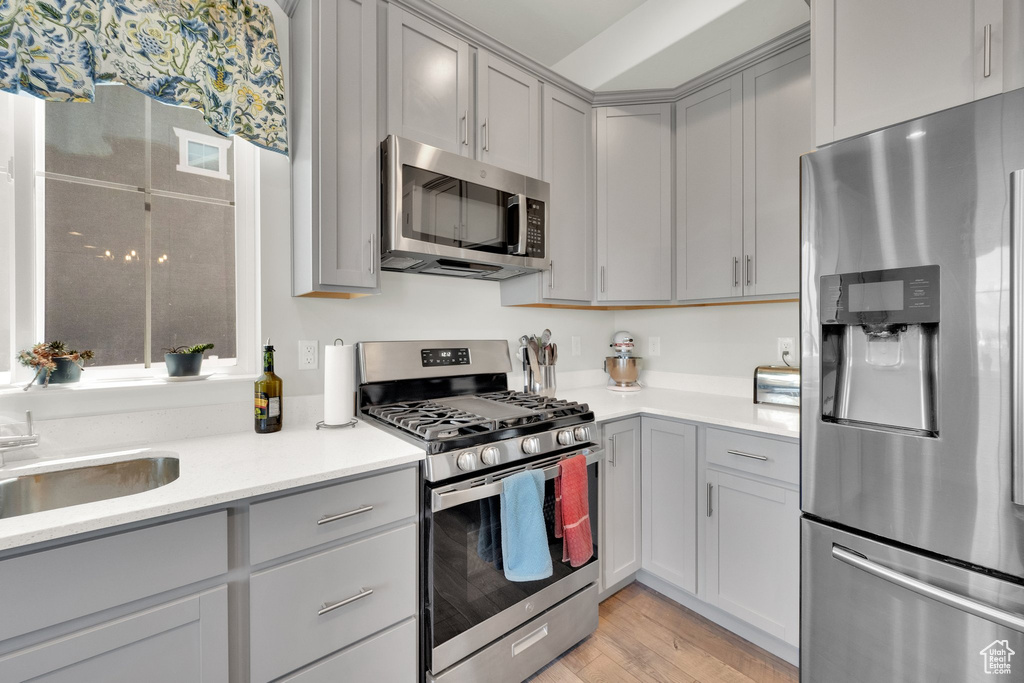 Kitchen featuring stainless steel appliances, gray cabinetry, light countertops, and light wood finished floors