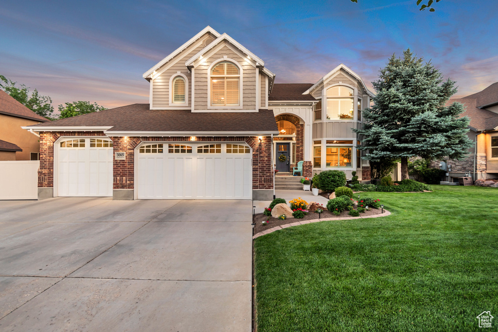 View of front of property featuring a front yard, concrete driveway, roof with shingles, brick siding, and a garage