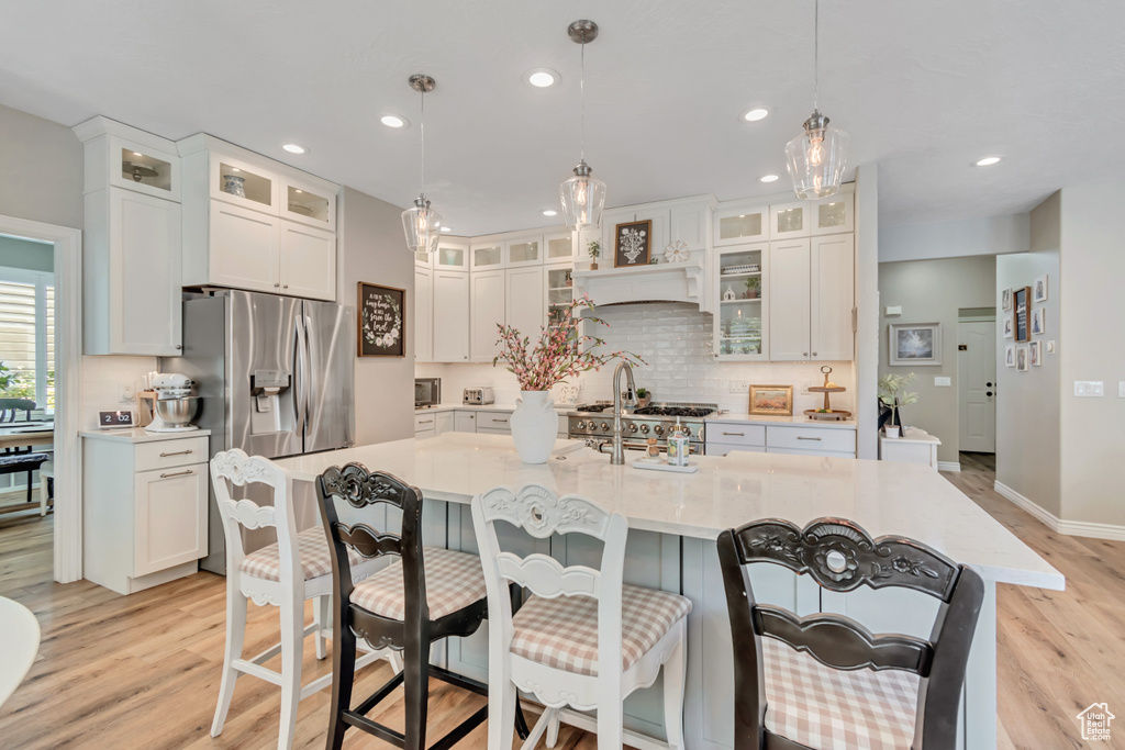 Kitchen featuring light wood-type flooring, backsplash, stainless steel refrigerator with ice dispenser, recessed lighting, and a breakfast bar