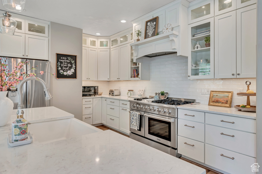 Kitchen featuring stainless steel appliances, light stone counters, decorative backsplash, white cabinets, and recessed lighting