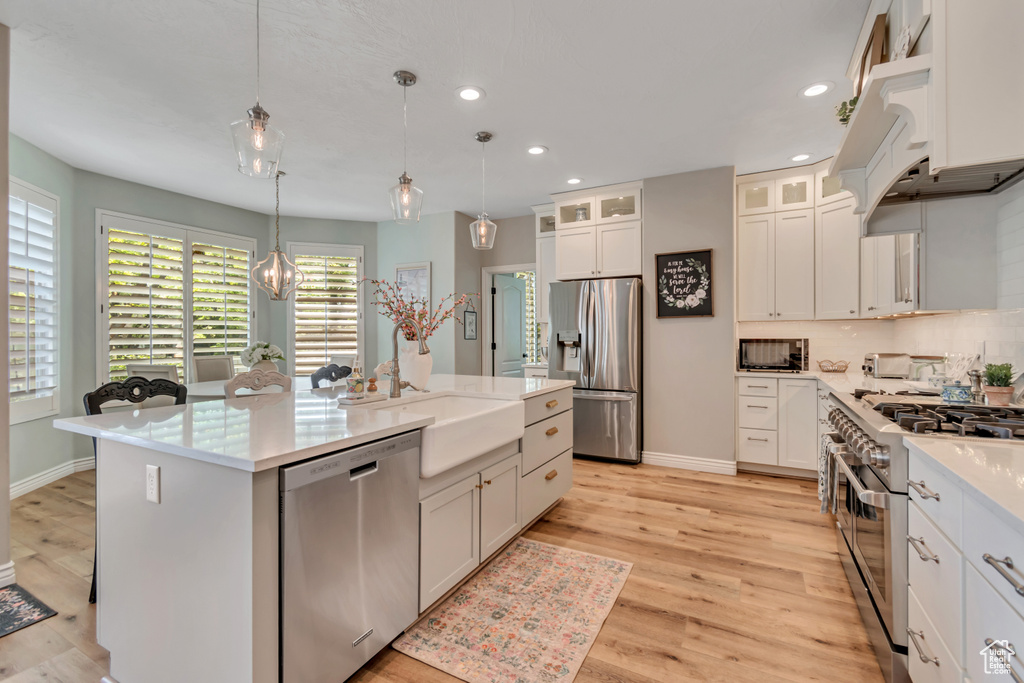 Kitchen with appliances with stainless steel finishes, recessed lighting, an island with sink, hanging light fixtures, and decorative backsplash