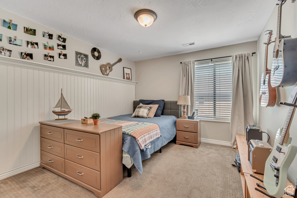 Bedroom featuring light carpet, a textured ceiling, and wainscoting
