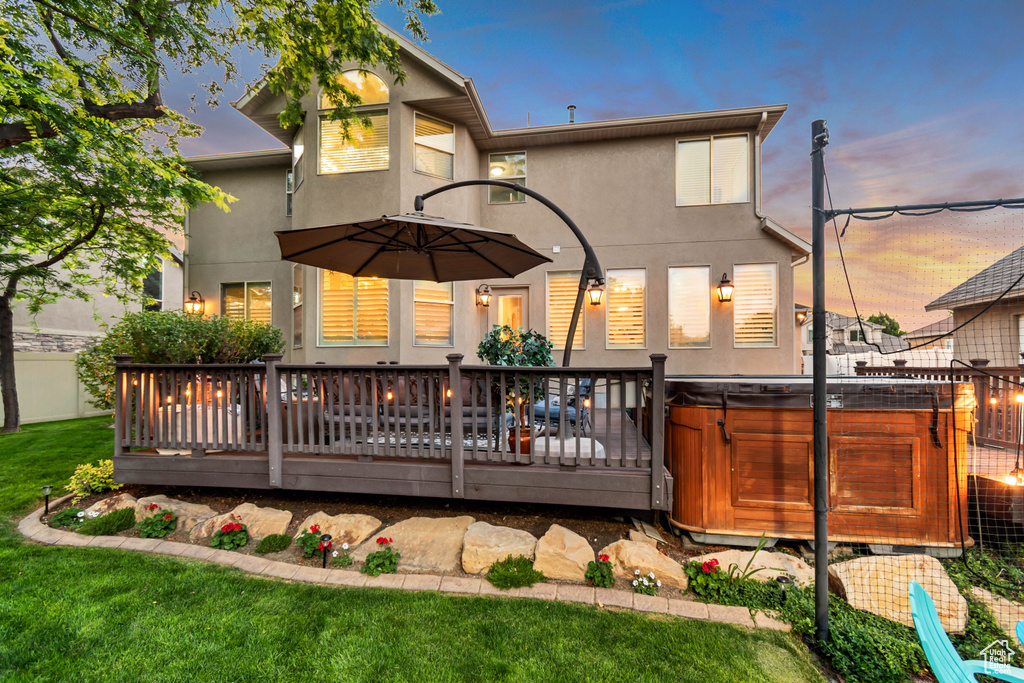 Back of house at dusk with a hot tub, stucco siding, and a wooden deck