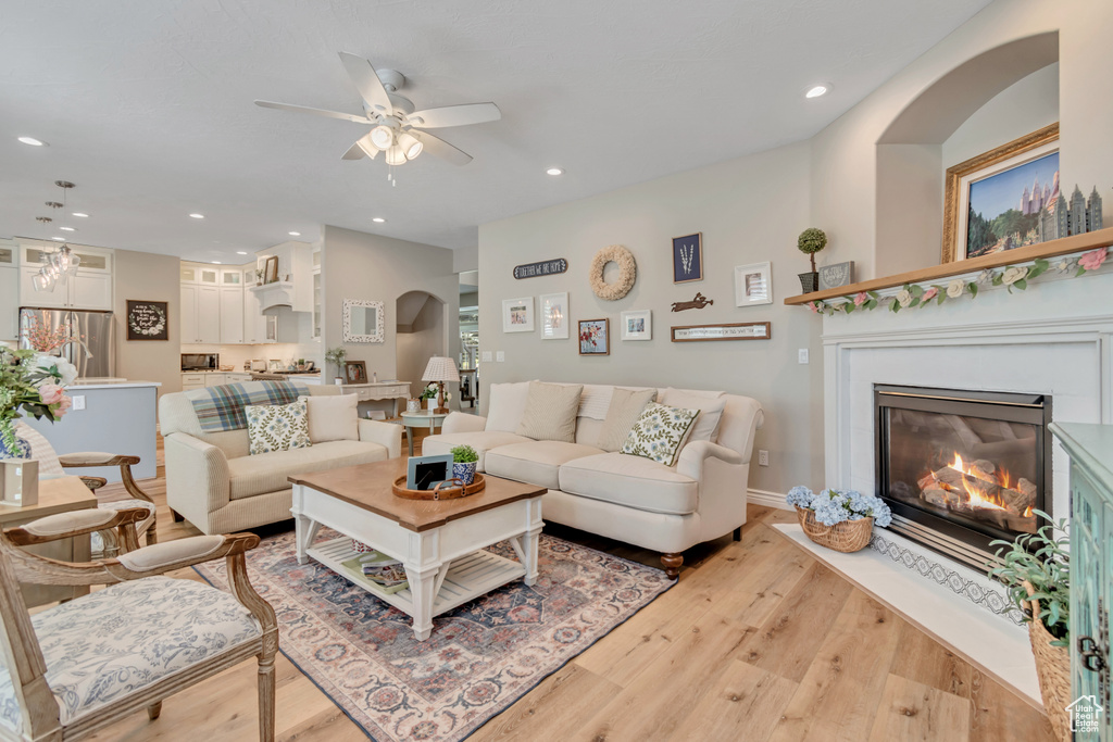 Living room featuring light wood-style flooring, a ceiling fan, a glass covered fireplace, and recessed lighting