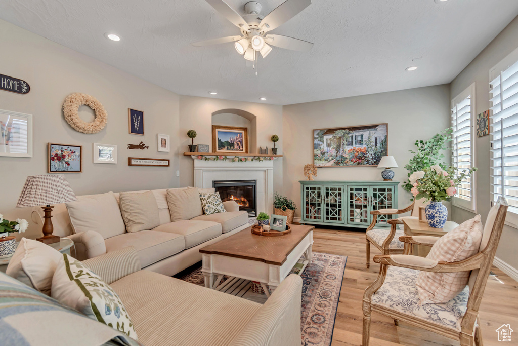 Living area with ceiling fan, a glass covered fireplace, wood finished floors, and recessed lighting