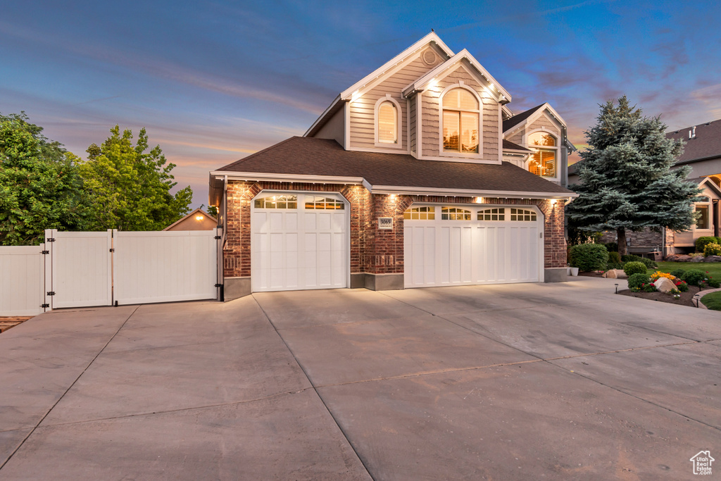 View of front of house with a gate, driveway, an attached garage, brick siding, and a shingled roof