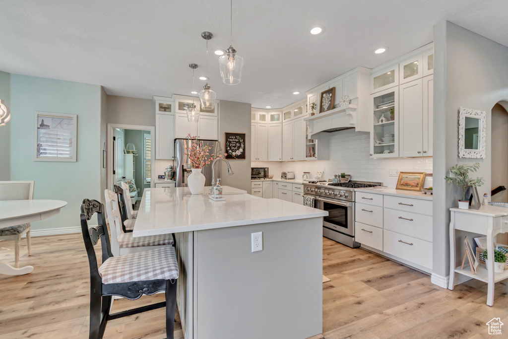 Kitchen with stainless steel appliances, custom range hood, light wood-type flooring, a kitchen breakfast bar, and recessed lighting