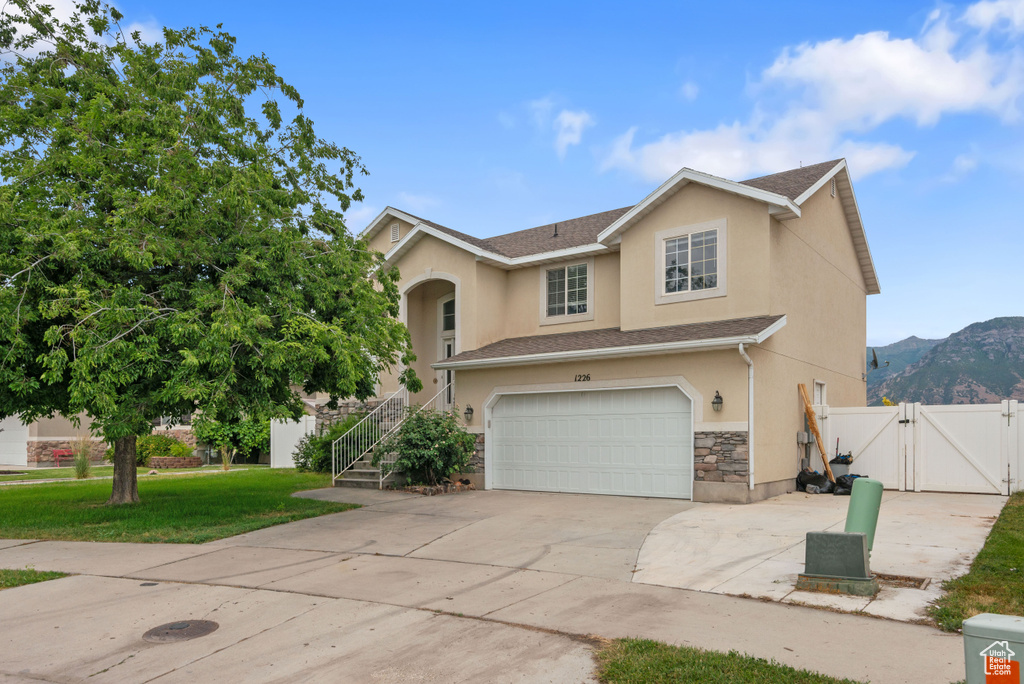 View of front facade featuring a gate, stucco siding, a garage, driveway, and stone siding