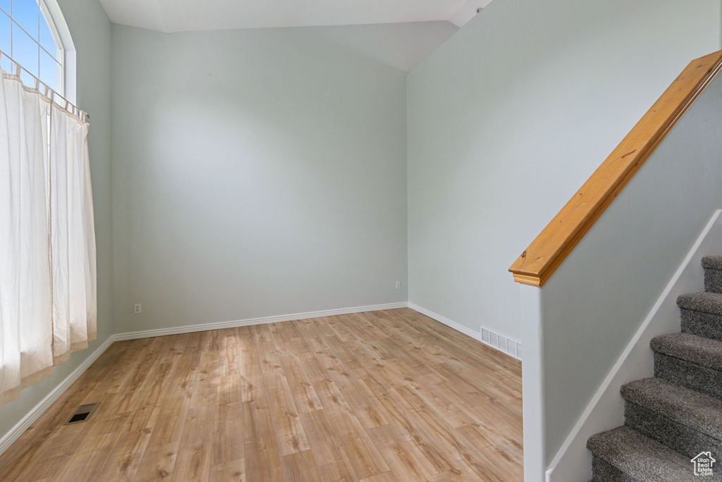 Empty room with stairs, light wood-type flooring, and lofted ceiling