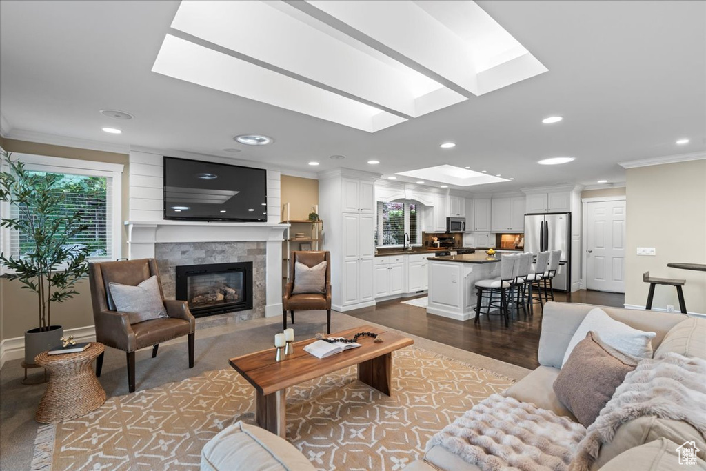 Living area with a skylight, recessed lighting, crown molding, a fireplace, and wood finished floors