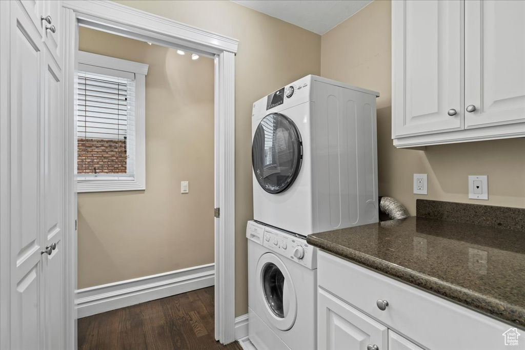 Laundry room with stacked washer / drying machine, dark wood finished floors, and cabinet space