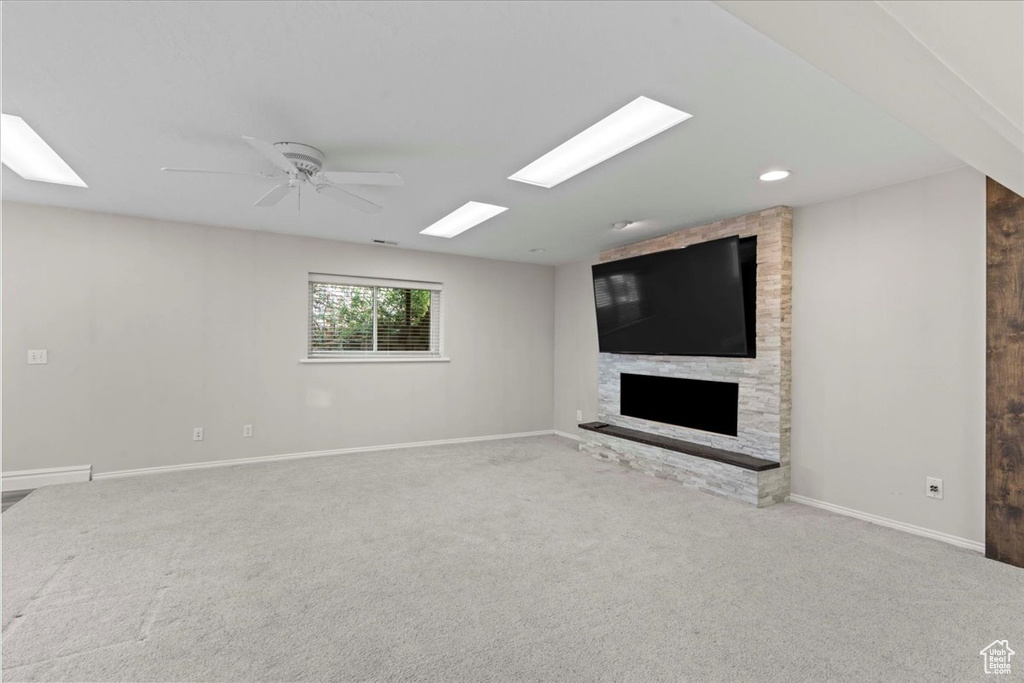 Unfurnished living room with carpet flooring, a stone fireplace, and a ceiling fan