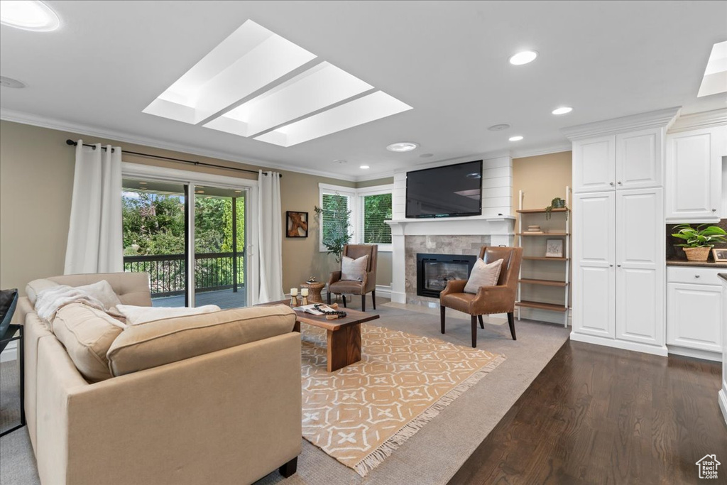 Living area with crown molding, a skylight, a glass covered fireplace, dark wood-style floors, and recessed lighting