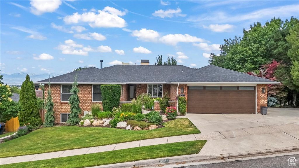 Ranch-style house with a garage, driveway, brick siding, a front lawn, and roof with shingles
