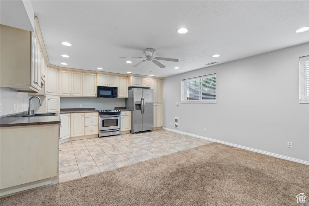 Kitchen with appliances with stainless steel finishes, light colored carpet, a ceiling fan, dark countertops, and recessed lighting