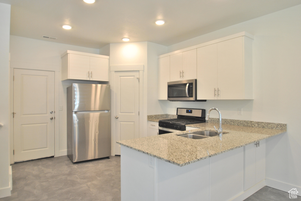 Kitchen with appliances with stainless steel finishes, a peninsula, light stone counters, white cabinetry, and recessed lighting