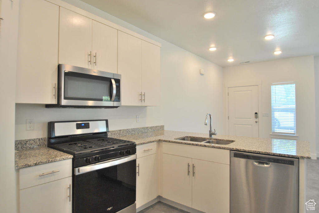 Kitchen with stainless steel appliances, a peninsula, recessed lighting, and light stone countertops