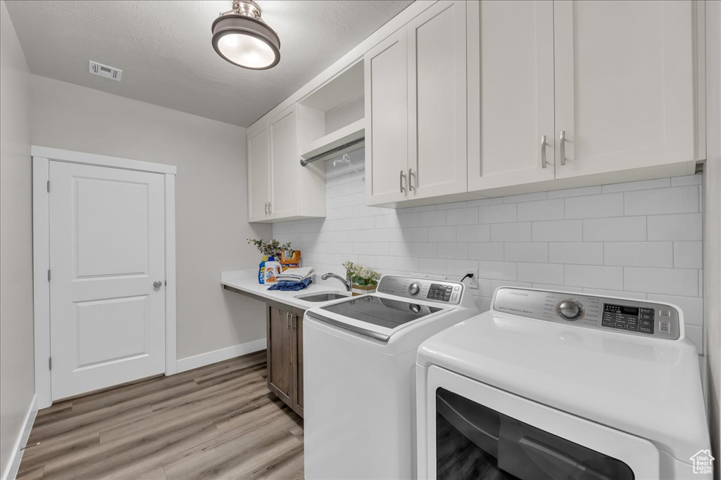 Washroom with cabinet space, washer and dryer, and light wood-style floors
