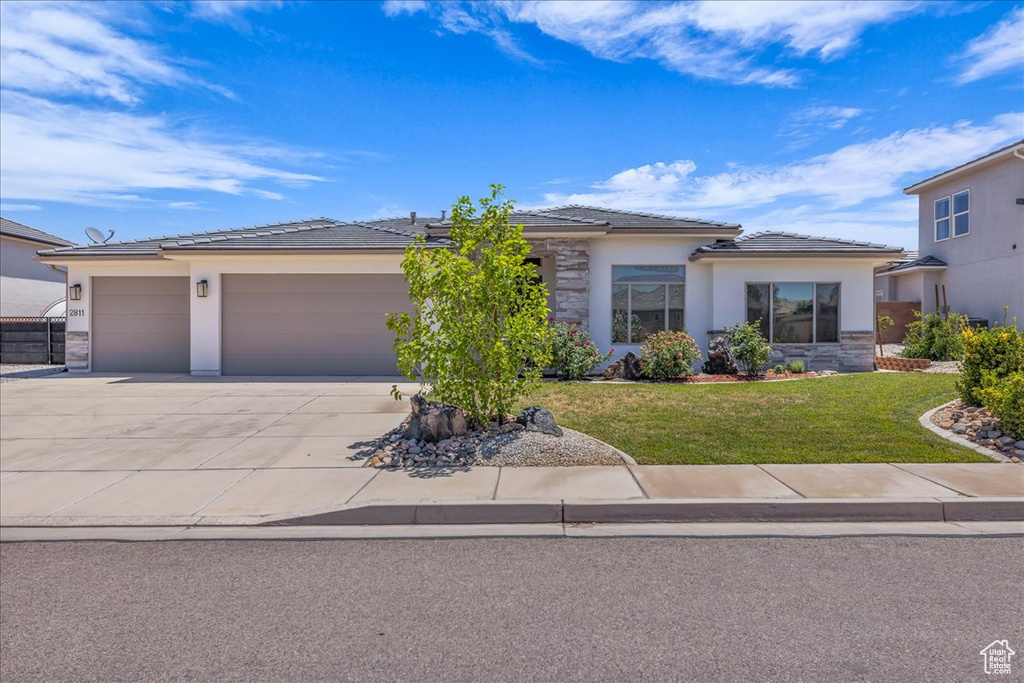 Prairie-style home featuring an attached garage, driveway, stucco siding, and a front yard