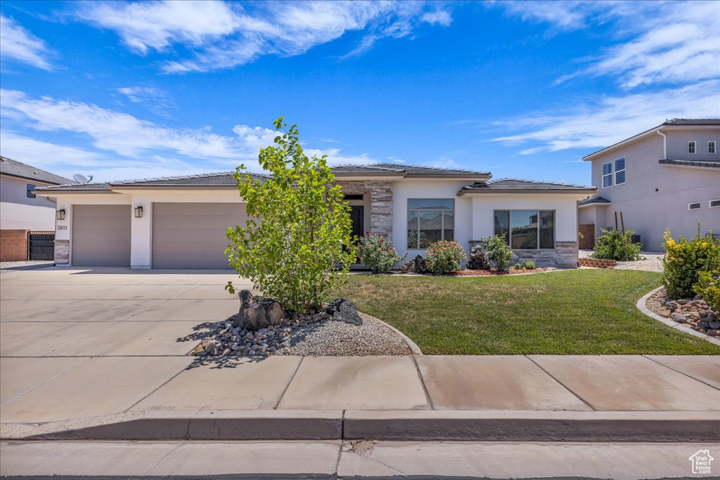 View of front facade with stucco siding, driveway, an attached garage, and a front yard