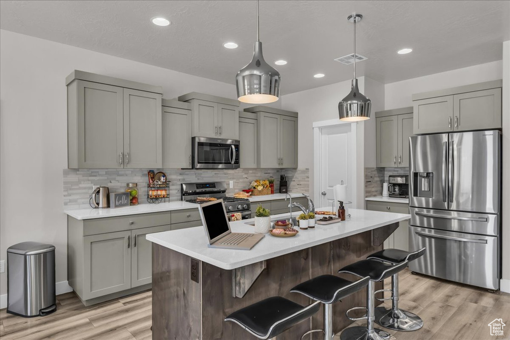 Kitchen with appliances with stainless steel finishes, gray cabinets, light wood finished floors, light countertops, and recessed lighting