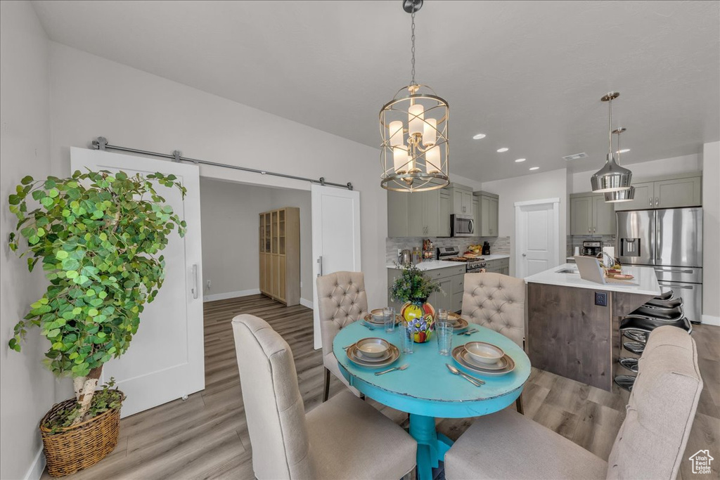 Dining room with a barn door, light wood-style flooring, a chandelier, and recessed lighting