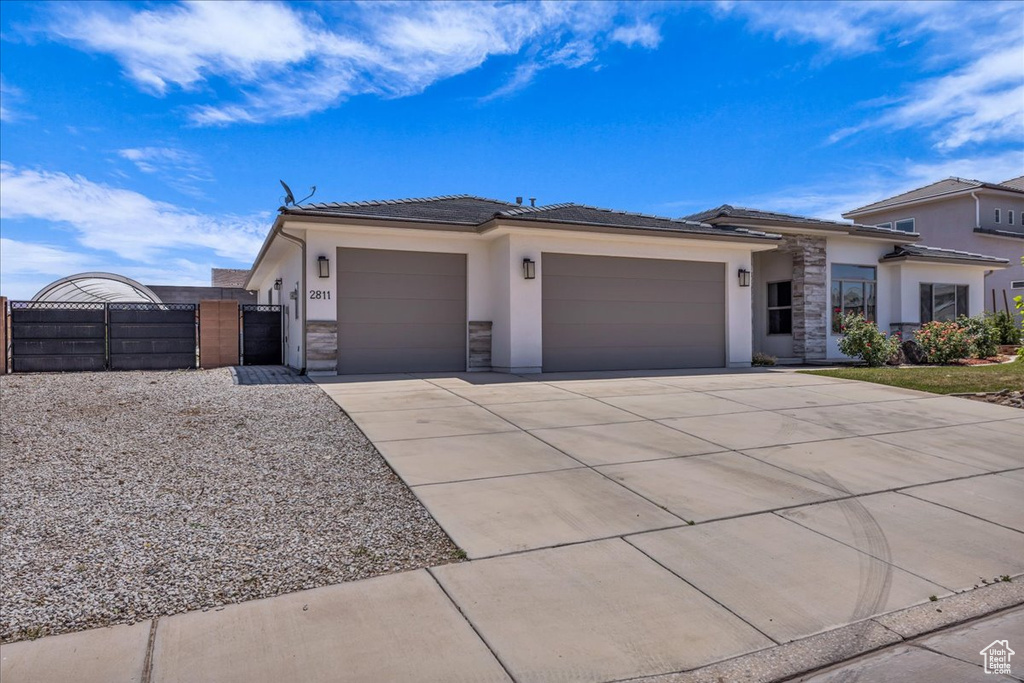 Prairie-style home featuring a gate, an attached garage, stone siding, stucco siding, and driveway